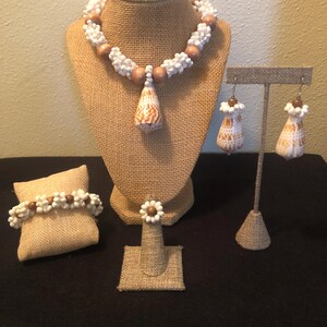 May include: A set of shell jewelry featuring a necklace, bracelet, ring, and earrings. The necklace and bracelet are made with white and brown beads, and the earrings and ring feature a brown shell with white markings.