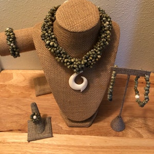 May include: A set of green shell jewelry including a necklace, bracelet, earrings, and ring. The necklace features a white bone pendant in the shape of a hook.