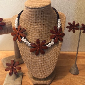 Könnte beinhalten: Ein Set aus braunem Holzblumen-Schmuck, bestehend aus einer Halskette, einem Armband, Ohrringen und einem Ring. Die Halskette und das Armband haben weiße Perlen, die zwischen den Holzblumen verteilt sind.