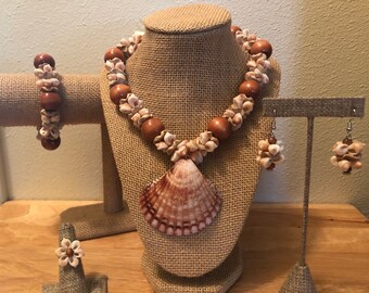 Könnte beinhalten: Ein Schmuckset aus Muscheln mit einer Halskette, einem Armband, Ohrringen und einem Ring. Die Halskette hat einen großen Muschel-Anhänger und ist aus braunen Holzperlen und kleinen weißen Muschelblüten gefertigt. Das Armband und die Ohrringe sind ebenfalls aus braunen Holzperlen und kleinen weißen Muschelblüten gefertigt.