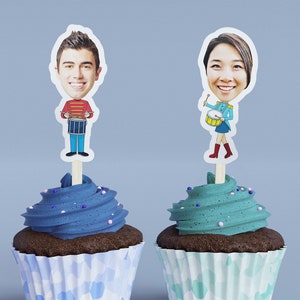 May include: Two cupcakes with blue and teal frosting, each topped with a personalized cartoon figure on a wooden stick. One figure is a man in a red and blue band uniform playing a drum. The other is a woman in a teal band uniform playing a drum.