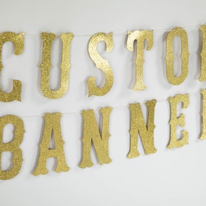 Puede incluir: Bandera de brillo dorado con las palabras "CUSTOM BANNER" en una fuente de estilo vintage.