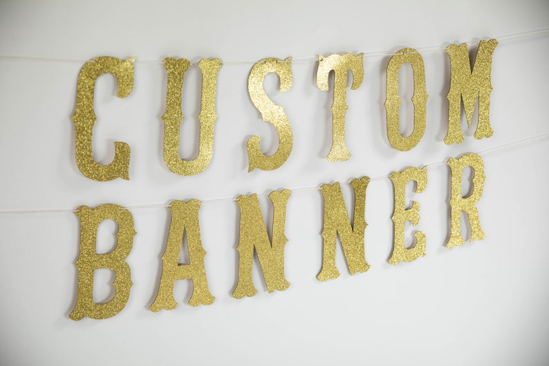 Puede incluir: Bandera de brillo dorado con las palabras "CUSTOM BANNER" en una fuente de estilo vintage.