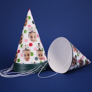 Peut inclure: Deux chapeaux de f&ecirc;te blancs avec une bordure verte. Un chapeau a un fond blanc avec des pois verts, roses et rouges et plusieurs images du visage d'une personne. L'autre chapeau est blanc uni.