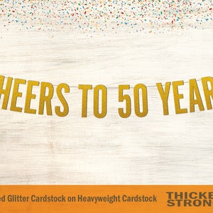 Peut inclure: Banni&egrave;re dor&eacute;e &agrave; paillettes avec le texte "CHEERS TO 50 YEARS". La banni&egrave;re est faite de papier cartonn&eacute; paillet&eacute; non-effiloch&eacute; sur papier cartonn&eacute; &eacute;pais. Le texte "THICKER & STRONGER" est imprim&eacute; en noir sur fond orange.