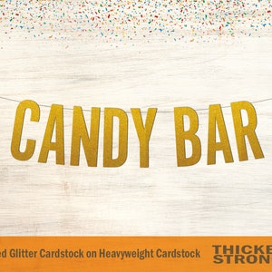 Peut inclure: Banni&egrave;re "CANDY BAR" en paillettes dor&eacute;es sur un fond en bois. La banni&egrave;re est faite de papier cartonn&eacute; paillet&eacute; non-effiloch&eacute; sur papier cartonn&eacute; &eacute;pais. Le texte "THICKER & STRONGER" est imprim&eacute; en noir en bas de l'image.
