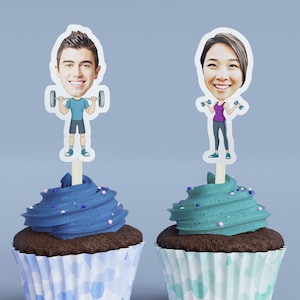 May include: Two cupcakes with blue and green frosting, topped with personalized cake toppers of cartoon figures holding weights. The figures are a man and a woman with exaggerated features.