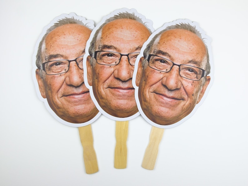May include: Three white cardboard face masks with a photo of an older man wearing glasses. The masks are attached to wooden sticks.