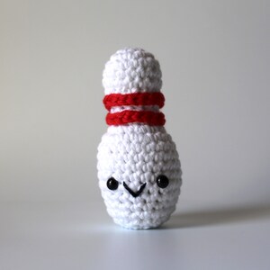 May include: White crocheted bowling pin with a red stripe around the middle and a black smiley face.