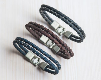 Puede incluir: Tres pulseras de cuero trenzado con cierres plateados. Las pulseras son de color azul marino, marrón y negro.