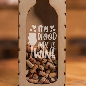 May include: Wooden wine cork holder shaped like a wine bottle, with the text "my blood type is wine." The holder is filled with wine corks. The background is blurred, with warm tones.