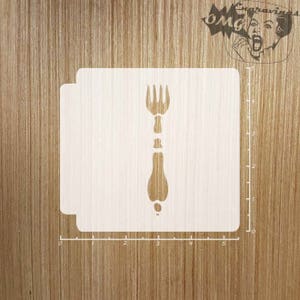 May include: A wooden stencil featuring a fork design. The stencil is light-colored and has a cutout of a fork with a detailed handle. The background is a light brown wooden surface. The stencil is approximately 5 inches wide.
