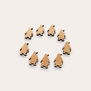 May include: A set of nine wooden penguin cutouts arranged in a circle. The penguins are all facing inwards, with their wings outstretched. The penguins are painted in a light brown color.