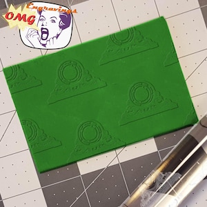 May include: A green rectangular object with a repeating pattern of a circular design within a triangle shape. The top left corner has a cartoon image with the word "OMG" and the word "Engravings".