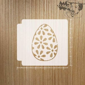 May include: A wooden stencil featuring an Easter egg design with a floral pattern. The stencil is light-colored and has a square shape with rounded corners. The image also includes a ruler for measurement.