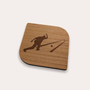 May include: A wooden coaster with a rounded corner design. The coaster features a dark brown silhouette of a bowler in action, with bowling lanes and a ball. The wood grain is visible, and the coaster has a black edge.