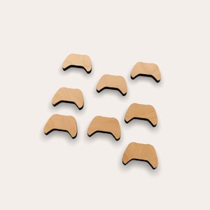 Puede incluir: Ocho mandos de juego de madera recortados en forma de mando de videojuego tradicional. Los mandos son todos del mismo tamaño y forma, y están dispuestos en un patrón escalonado.