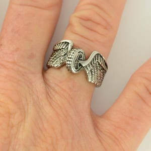 May include: A silver ring with a motorcycle wheel design and wings on either side.