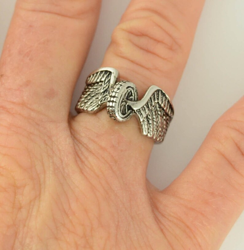 May include: A silver ring with a motorcycle wheel design and wings on either side.