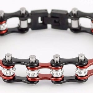 May include: A bracelet with a bicycle chain design. The bracelet features alternating black and red links, with silver-colored accents. Some links are adorned with small, clear crystals. The clasp is black.