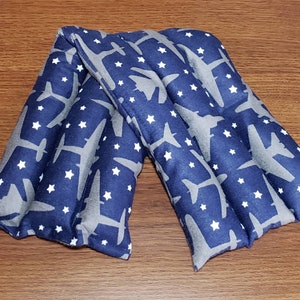 May include: A blue and gray fabric neck wrap with a pattern of white stars and gray airplanes. The wrap is folded in half and is lying on a wooden surface.