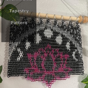 Peut inclure: Une tapisserie en chainmaille noire et blanche avec un motif de fleur rose. La tapisserie est suspendue à une tringle en bois avec des crochets argentés.