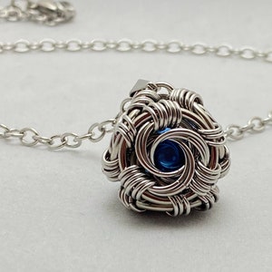 May include: A silver chain necklace with a silver wire-wrapped pendant featuring a blue gemstone in the center.
