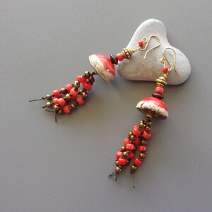 May include: A pair of red and gold earrings with ceramic mushroom-shaped charms and dangling beads.