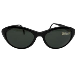 May include: Black cat-eye sunglasses with dark lenses. The sunglasses have a sleek, curved frame and a small white sticker with the text "Calvin Klein". The sunglasses are a classic accessory.
