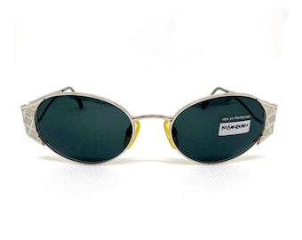 May include: Silver oval sunglasses with dark green lenses and a YSL logo on the right lens. The sunglasses have a 100% UV protection label.