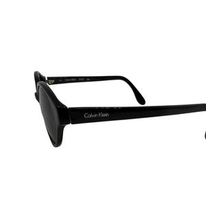 May include: Black Calvin Klein sunglasses with a rectangular frame and dark lenses. The brand name is visible on the temple. The sunglasses are set against a white background.