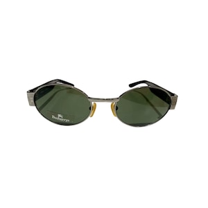 Peut inclure: Lunettes de soleil ovales argentées avec des verres verts et un logo Burberry sur la lentille gauche.