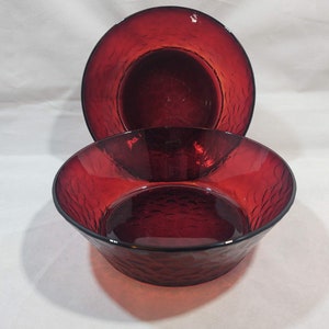 May include: Two red glass bowls with a textured surface. The bowls are stacked on top of each other.
