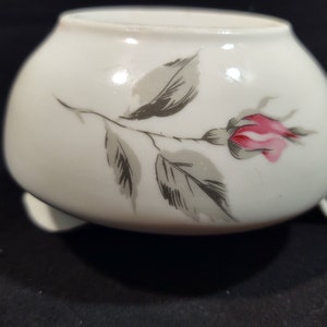 Può includere: Un creamer in ceramica bianca con un delicato design di rosa grigia e rosa. Il creamer ha un corpo arrotondato e un piccolo manico.