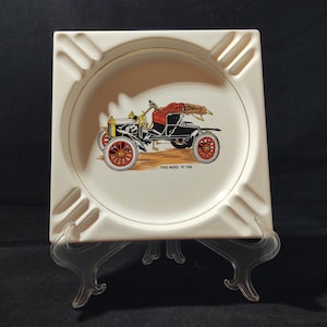 Puede incluir: Cenicero de cerámica blanca con borde dorado y una ilustración vintage de un Ford modelo 'N' 1906 negro. El cenicero tiene tres hendiduras para cigarrillos.