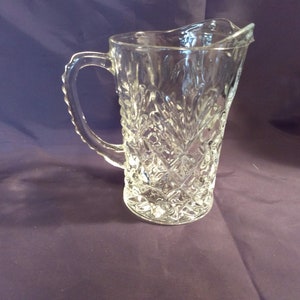 May include: A clear glass pitcher with a diamond pattern. The pitcher has a handle and a wide mouth.