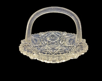 May include: Clear glass basket with a handle. The basket has a scalloped edge and a detailed, geometric pattern. The handle is arched and textured. The basket is likely used for serving or display.