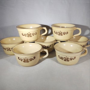 Puede incluir: Juego de seis tazas de cerámica de color crema con diseños florales marrones y bordes marrones. Las tazas tienen una forma redondeada y un asa en el lateral.