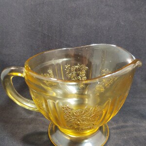 May include: A yellow glass creamer with a floral design and a footed base.