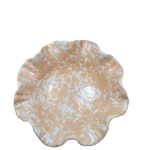 May include: A decorative bowl with a ruffled edge. The bowl has a peach-coloured base with white splatter-like patterns. The rim of the bowl has a light blue accent. This bowl is ideal for serving or display.
