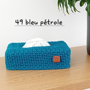 Op de afbeelding: Een rechthoekige tissueboxhoes gehaakt van petrolblauw garen. De hoes heeft een centrale opening waar een witte tissue uitsteekt en een klein bruin lederachtig label aan de rechtervoorkant met de tekst Maille Home erop gedrukt.