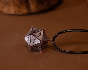May include: A silver and black d20 dice charm on a black cord necklace. The dice is a 20-sided die with numbers 1 through 20 on each side. The necklace is a simple black cord with a silver clasp.