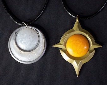 May include: Two pendant necklaces on black cords. One features a silver-colored, layered circular design with a textured, white inner circle. The other has a gold-colored, starburst-shaped pendant with an orange, spherical center.