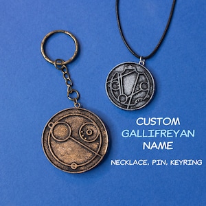 May include: Two silver and bronze Gallifreyan symbol pendants, one on a black cord necklace and the other on a silver key chain. The text below reads "CUSTOM GALLIFREYAN NAME NECKLACE, PIN, KEYRING".