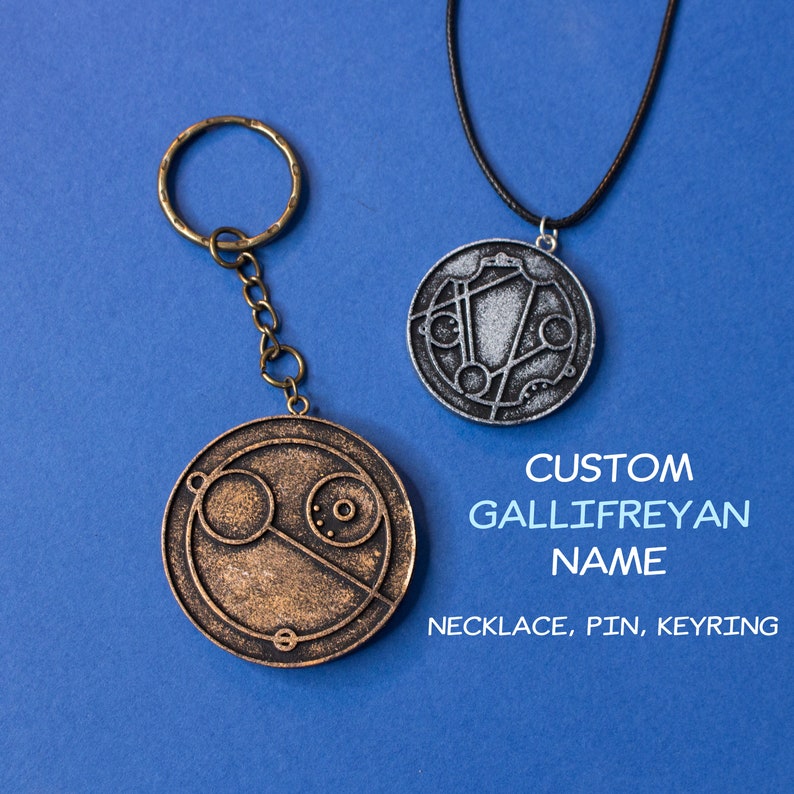 May include: Two silver and bronze Gallifreyan symbol pendants, one on a black cord necklace and the other on a silver key chain. The text below reads "CUSTOM GALLIFREYAN NAME NECKLACE, PIN, KEYRING".