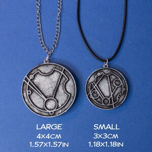 May include: Two silver necklaces with circular pendants featuring a geometric design. The larger pendant measures 4x4 cm and the smaller pendant measures 3x3 cm.