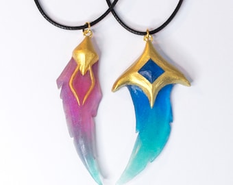 May include: Two necklaces with pendants shaped like stylised wings. One pendant is pink and blue, the other is blue and green. Both pendants have gold accents.