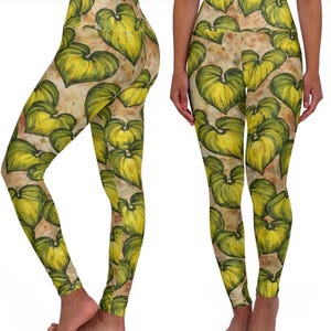 Könnte beinhalten: Hoch taillierte Leggings mit einem sich wiederholenden Muster aus großen, stilisierten gelb-grünen Blättern auf einem gesprenkelten, hellbraunen Hintergrund. Die Leggings sind figurbetont und aus einem dehnbaren Material gefertigt.