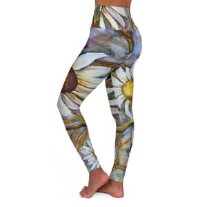 May include: High-waisted leggings featuring a watercolor-style print of large white daisies with yellow centers and brown accents. The floral pattern covers the entire garment, showcasing overlapping petals and stems in shades of white, yellow, brown, and muted blue.