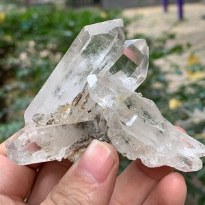 Pode incluir: Um aglomerado de cristais de quartzo transparentes com uma textura áspera e natural. Os cristais estão dispostos em um aglomerado, alguns apontando para cima e outros para baixo. Os cristais são translúcidos e têm um leve brilho.
